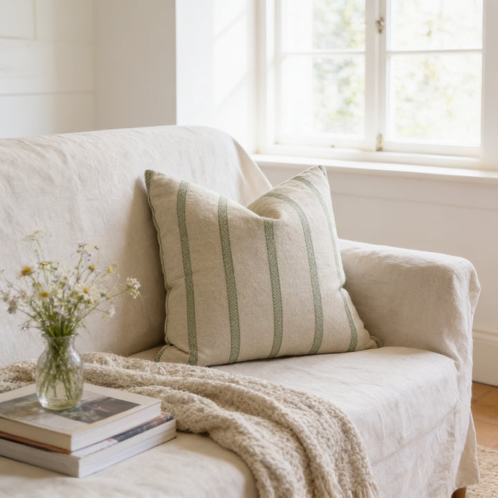 A cozy living room with a beige sofa, a striped pillow, and a vase of flowers on a coffee table.