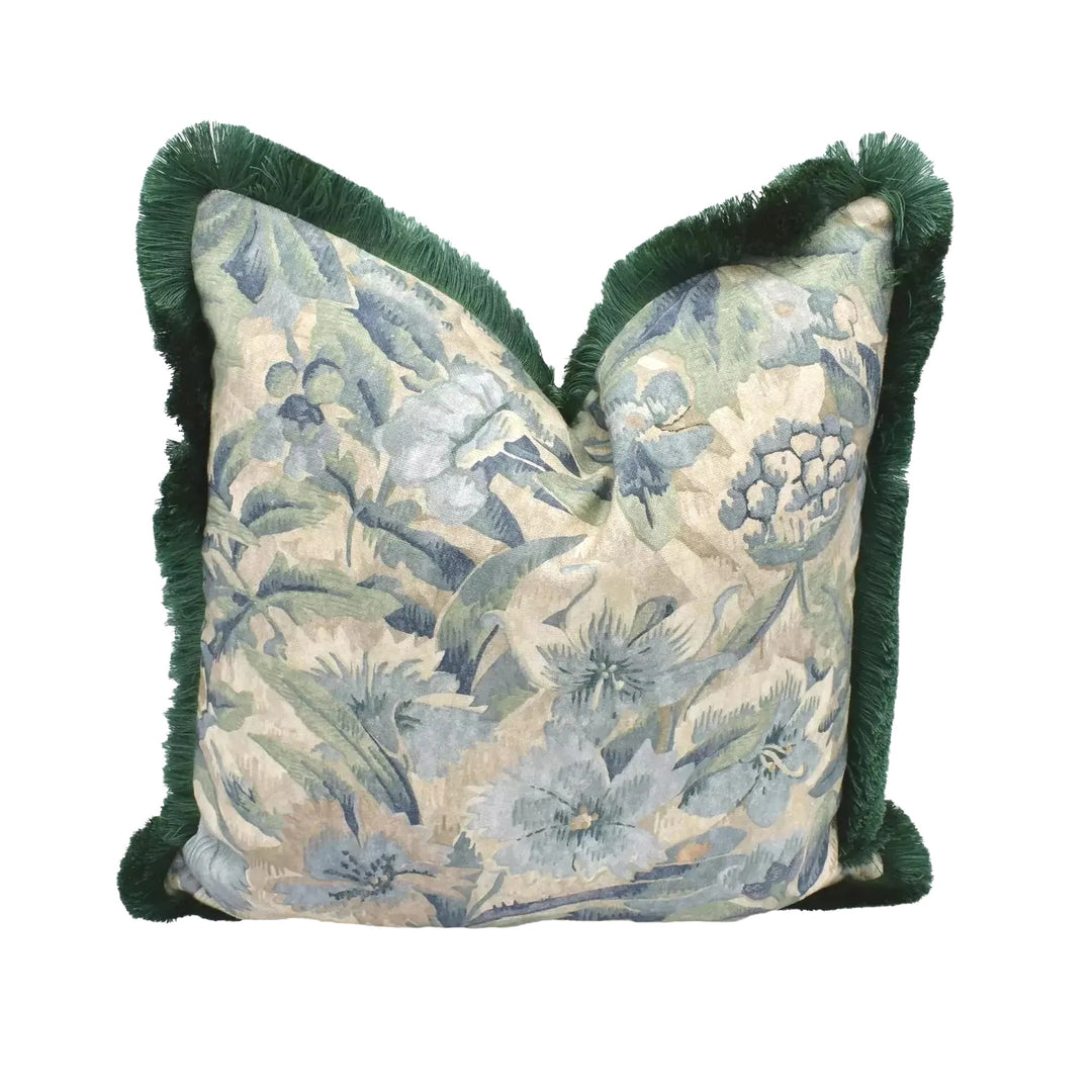 A decorative throw pillow with a floral print and green fringe is displayed against a white background.