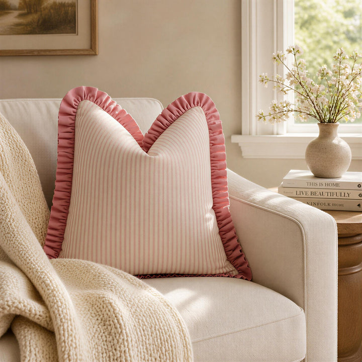 A cozy living room with a white sofa adorned with a pink and white striped pillow, a white blanket, and a vase of flowers on a windowsill.