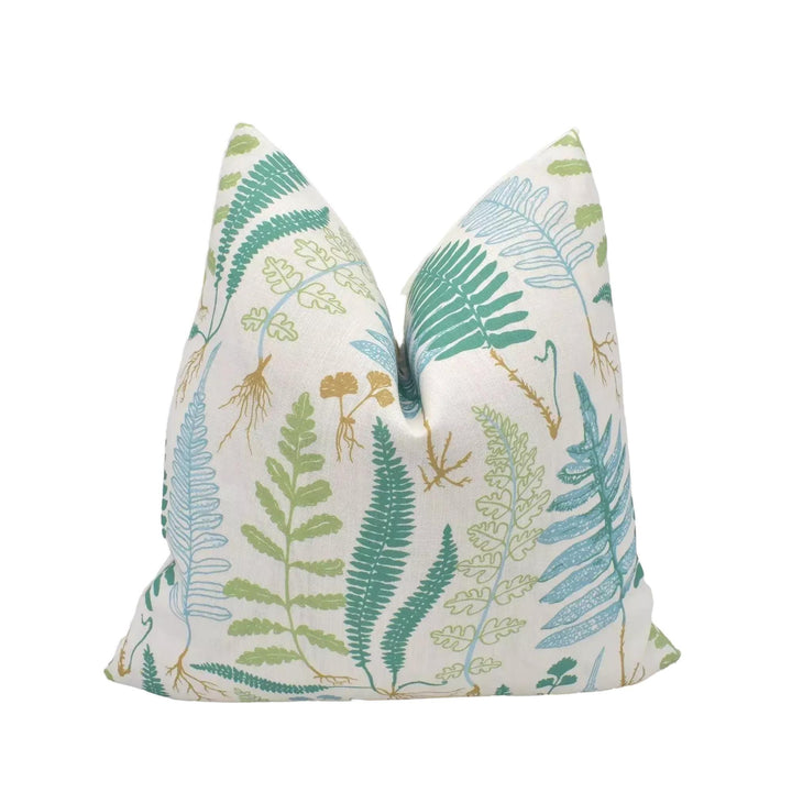 A white pillow with a pattern of green and blue ferns and other plants, placed against a white background.