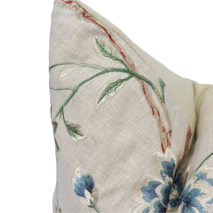 A close-up view of a beige fabric with a floral pattern, featuring green and blue flowers and leaves.