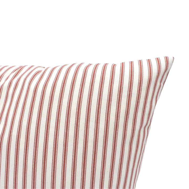 A close-up view of a red and white striped pillow against a plain white wall.
