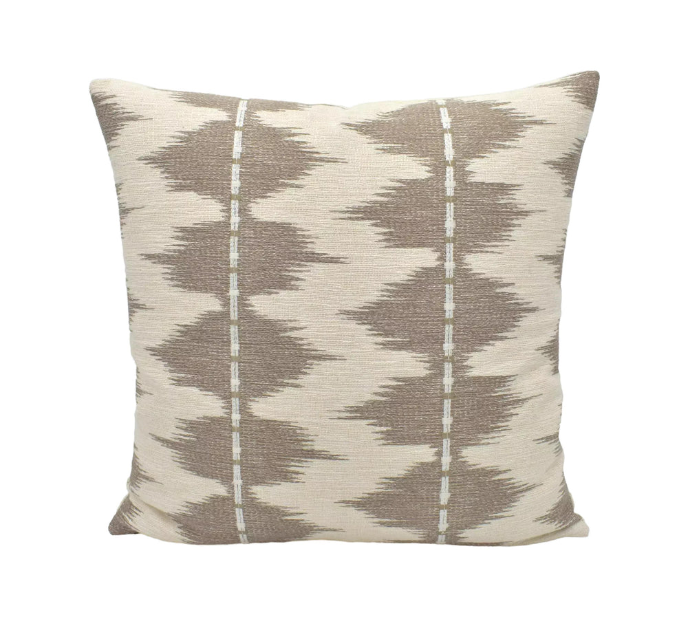 A beige and brown patterned throw pillow is displayed against a white wall.