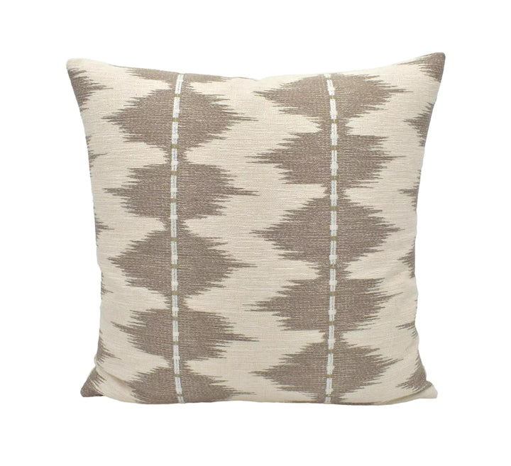 A beige and brown patterned throw pillow is displayed against a white wall.