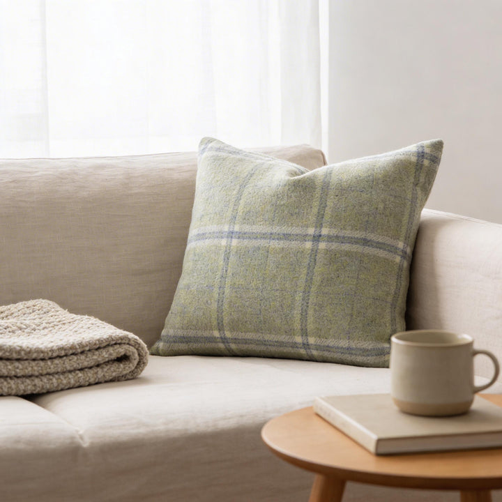 a cozy living room with a beige sofa, a green and white plaid throw pillow, a white mug, and a book on a small wooden side table.