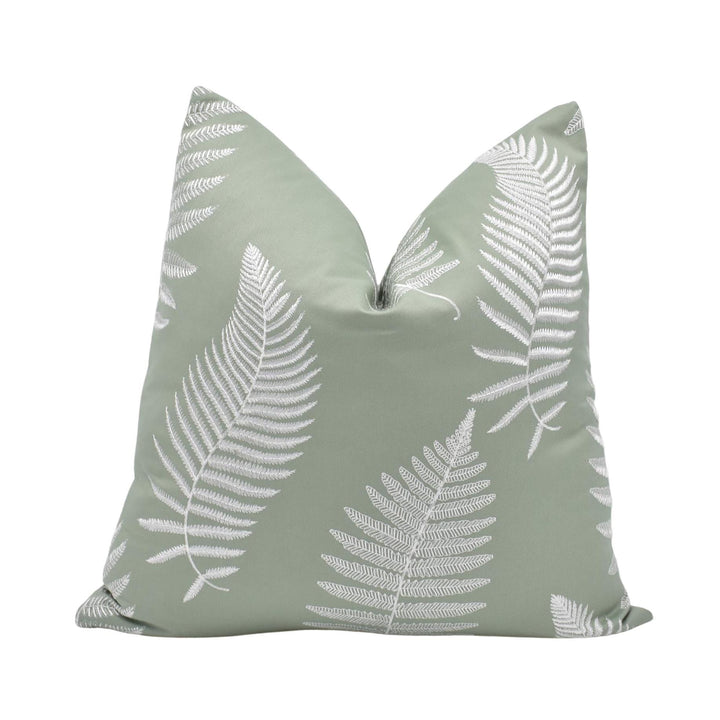 A green throw pillow with white fern leaf patterns.