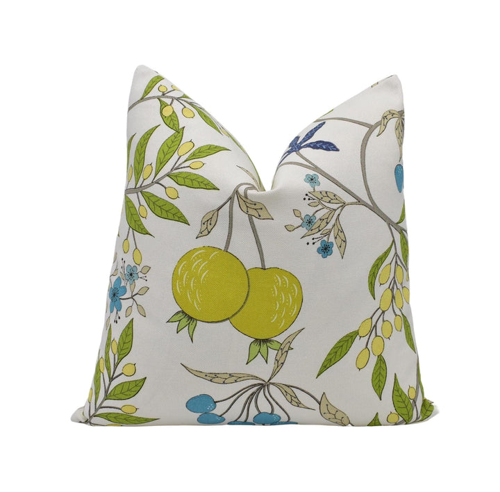 a white pillow with a floral pattern of green leaves, yellow fruits, and blue flowers.