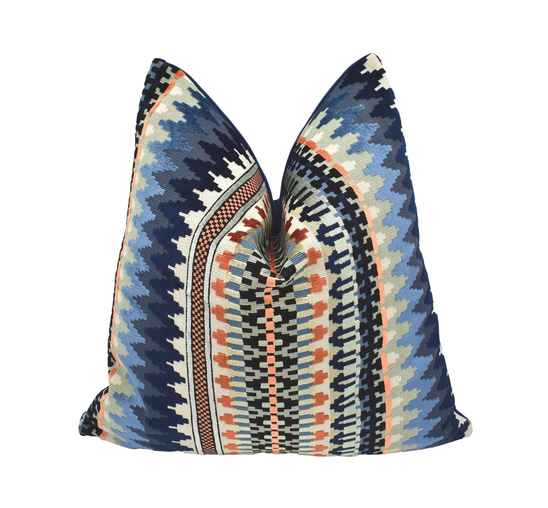 a decorative pillow with a vibrant, colorful pattern of stripes and geometric shapes in shades of blue, orange, and gray.