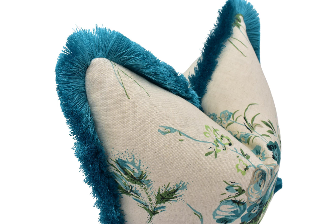 A close-up image of a decorative pillow with a floral pattern and a blue fringe trim.
