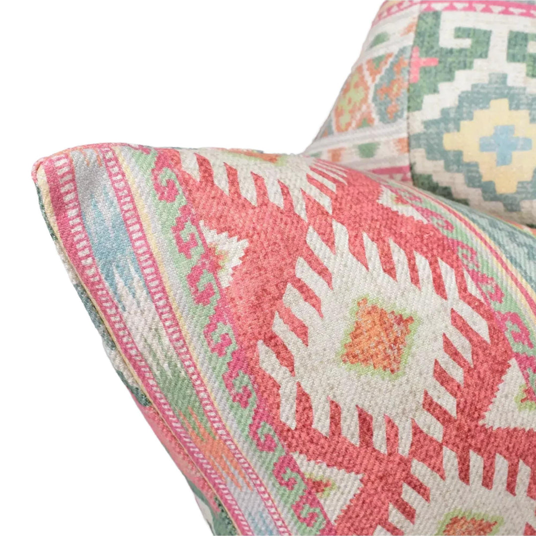 a close-up view of a vibrant, patterned pillow with a mix of pink, green, and orange colors. The pillow appears to be made of a soft, textured fabric, and it has a geometric design with a repeating pattern of shapes and lines.