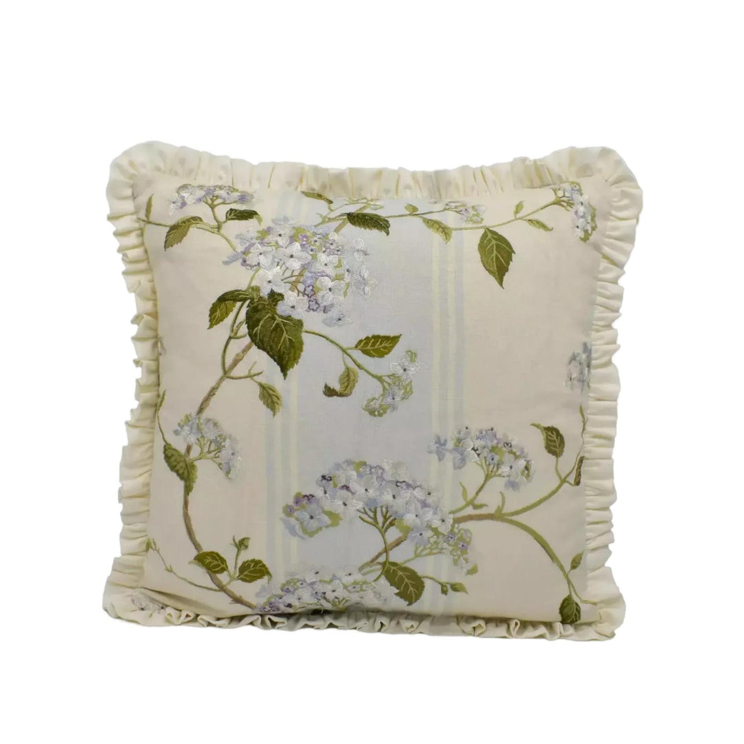 A decorative white pillow with a floral pattern of white and green flowers, along with green leaves, is shown against a white background.