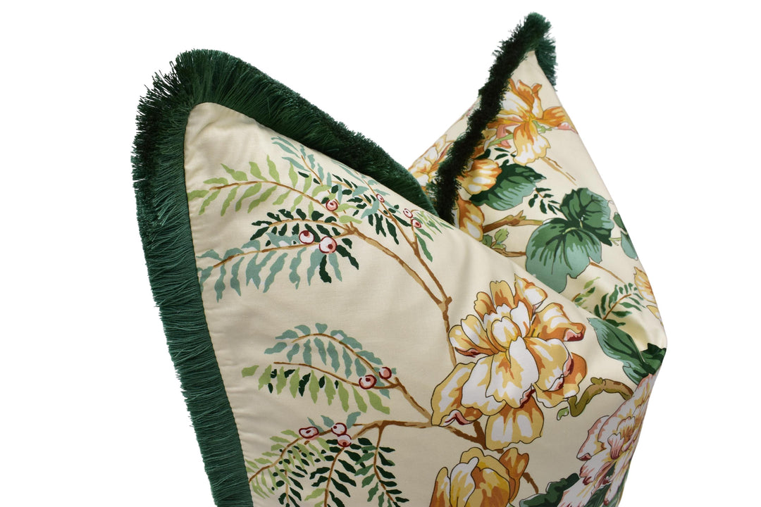 a close-up view of a decorative pillow with a floral pattern. The pillow has a green fringe on the edges and a beige background with a floral design.