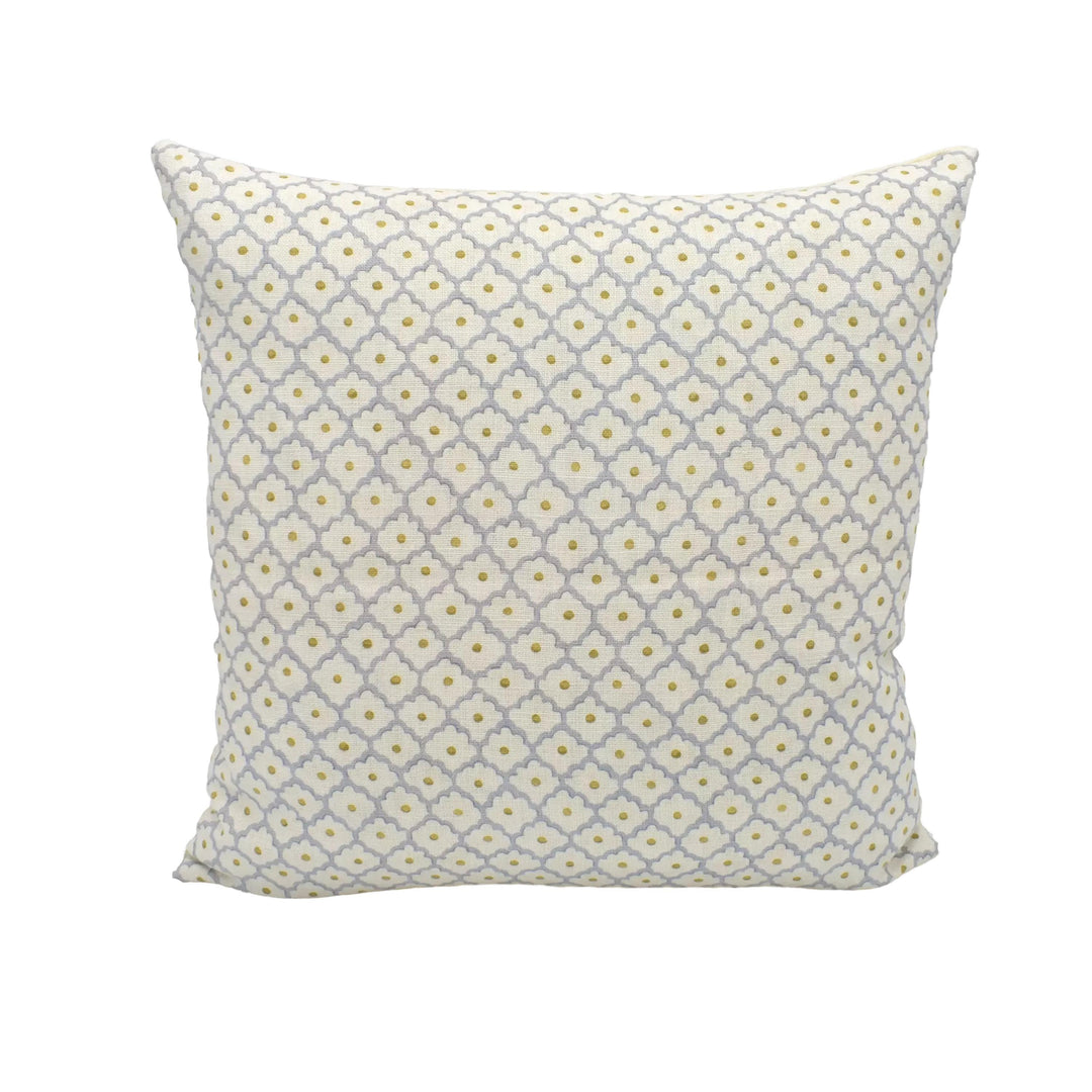 A square throw pillow with a repeating pattern of yellow and gray flowers is placed against a white wall.