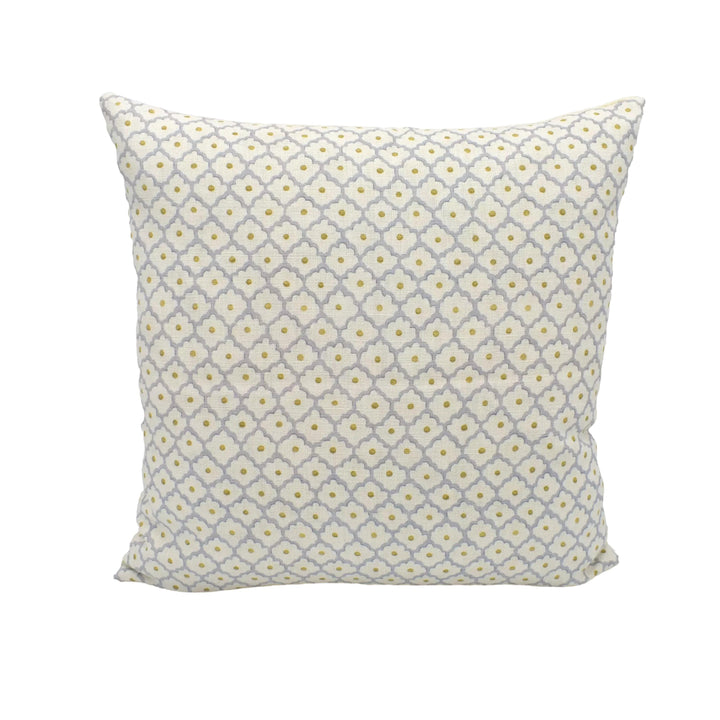 A square throw pillow with a repeating pattern of yellow and gray flowers is placed against a white wall.