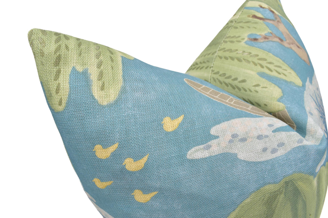 A close-up view of a blue and green fabric pillow with a pattern of yellow birds and green leaves.