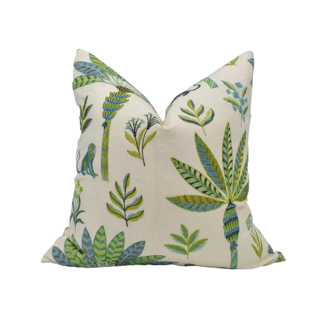 a decorative pillow with a tropical theme, featuring various plants and leaves in shades of green and blue.