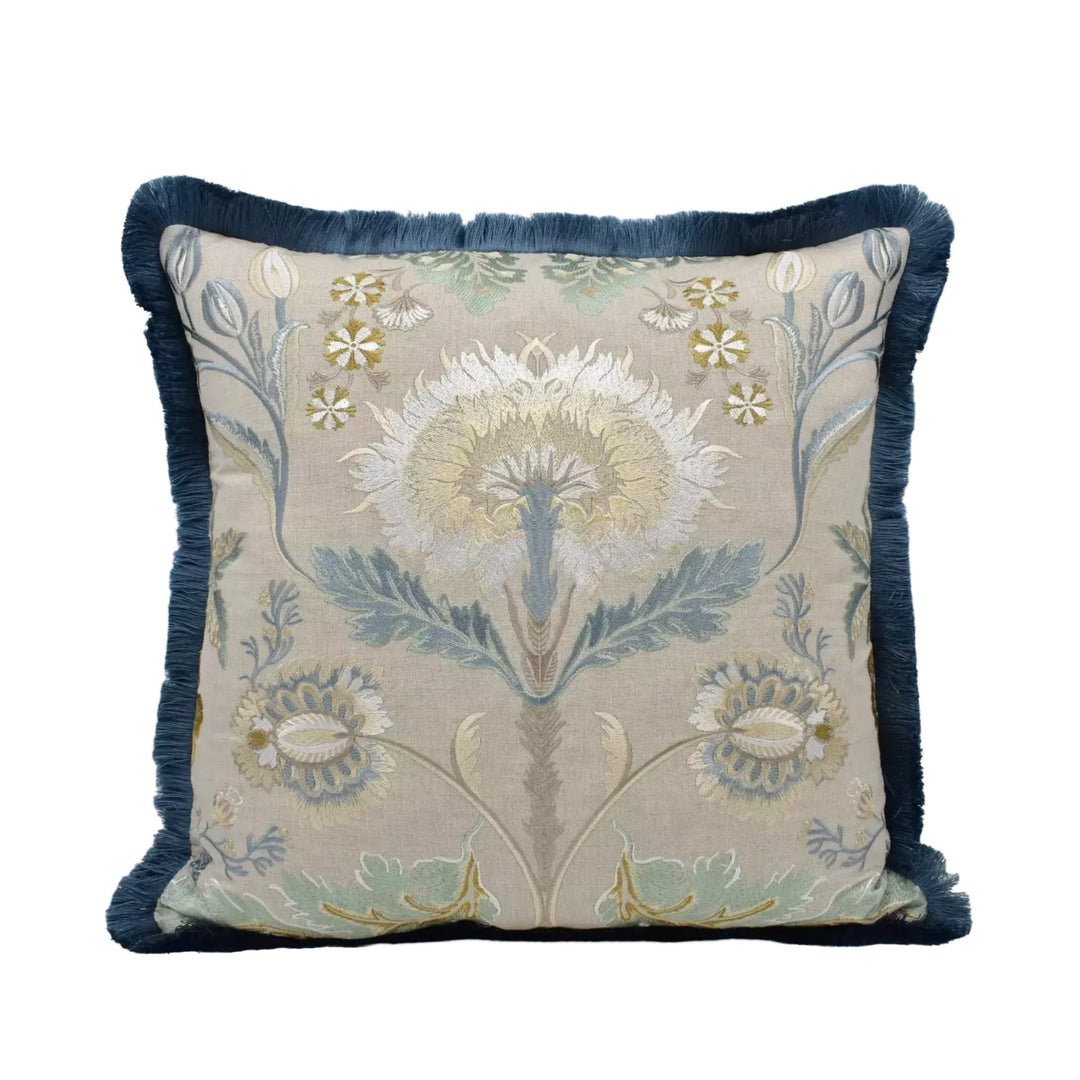 A decorative throw pillow with a floral pattern in shades of blue, green, and white. The pillow has a blue trim and a fringed edge, giving it a classic and elegant appearance.