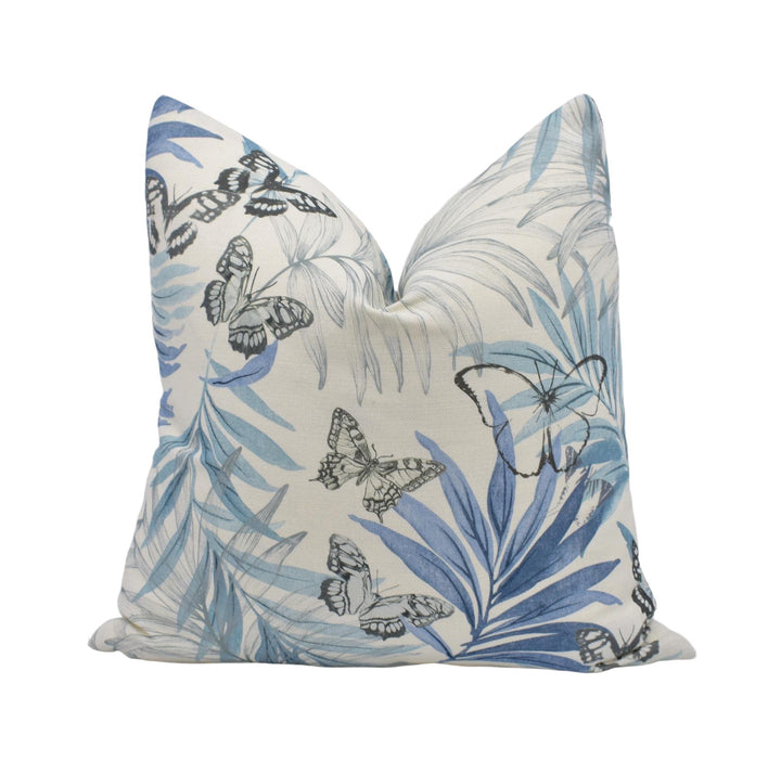 a decorative pillow with a tropical leaf and butterfly pattern in shades of blue and white.
