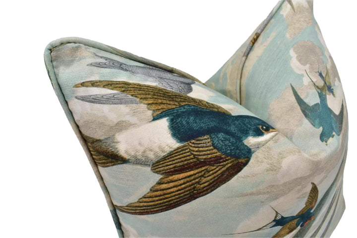 a close-up view of a decorative pillow with a pattern of flying birds, including a blue bird with a green head and wings.