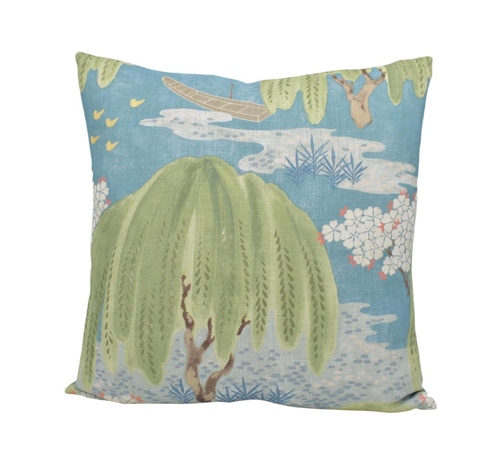 a square throw pillow with a vibrant, nature-inspired design. The pillow has a blue background with a lush green tree and a small boat floating on a body of water. The design is detailed and colorful, creating a visually appealing and decorative piece.