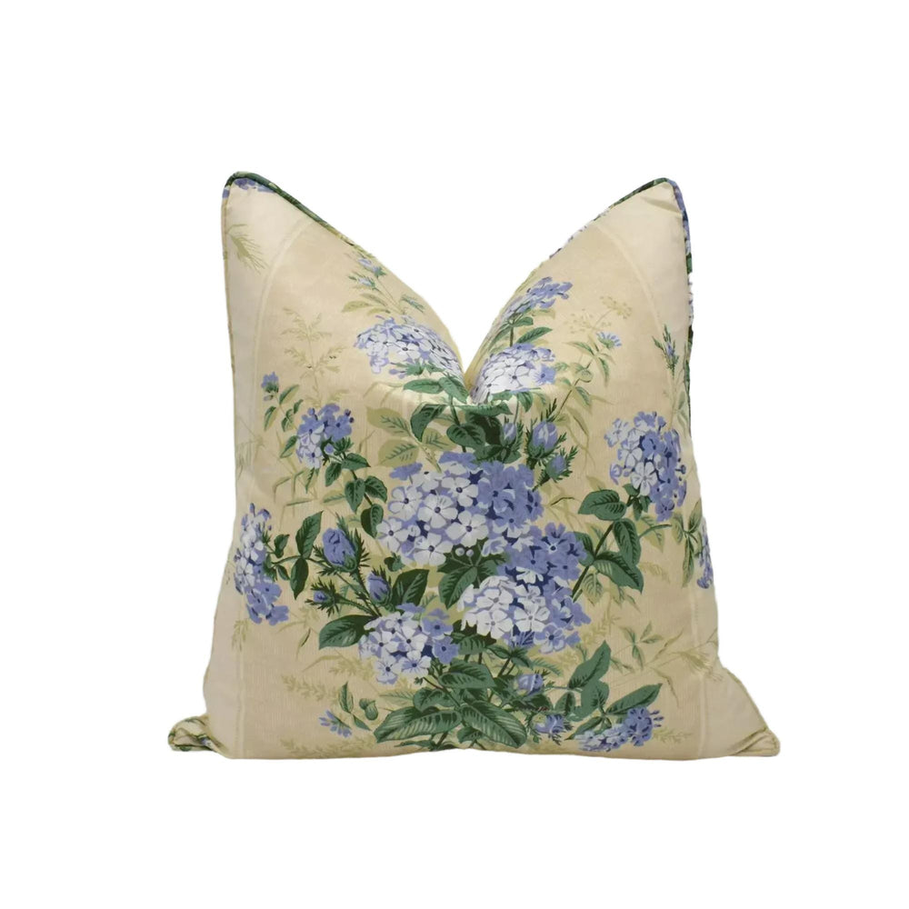 A beige pillow with a floral print of blue hydrangeas and green leaves.